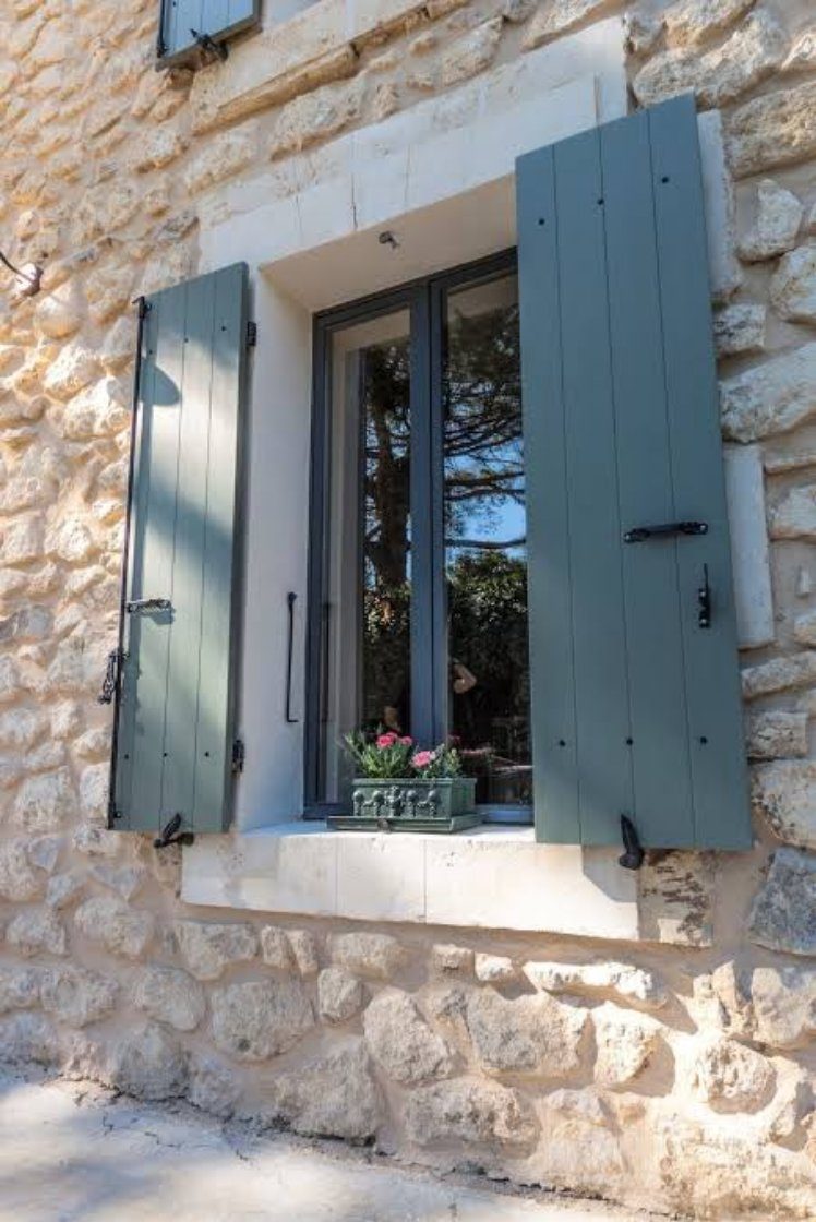Volets battants en bois peints vert de gris sur une façade en pierre, avec fenêtre aluminium anthracite